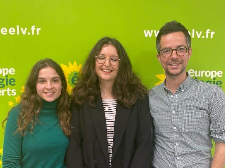 Ophélie Madinier, Camille Laffitte et Maxime Crosnier, l'air décontracté, sourient devant un fond vert et jaune aux couleur EELV. Ce sont les responsables du pôle "accueil et formation" du BED de EELV Paris.