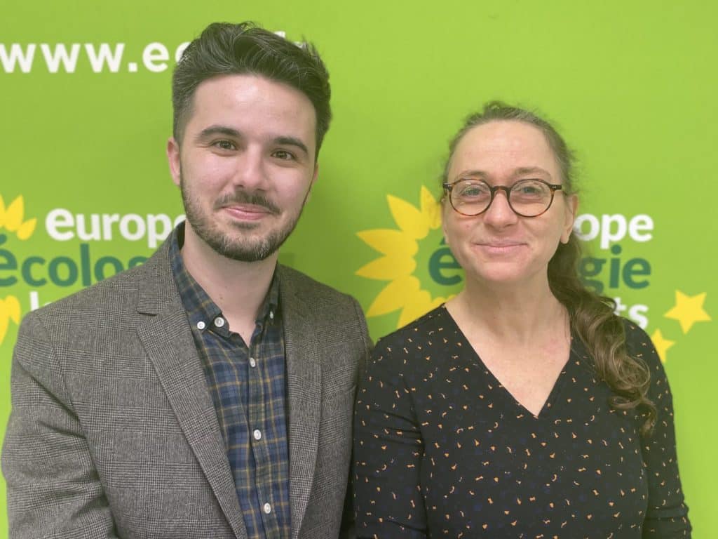 Les deux co-secrétaires du BED de EELV Paris, Antoine Alibert (jeune homme brun) et Charlotte Nenner,(femme aux longs cheveux) devant un fond vert et jaune aux couleurs de EELV Paris