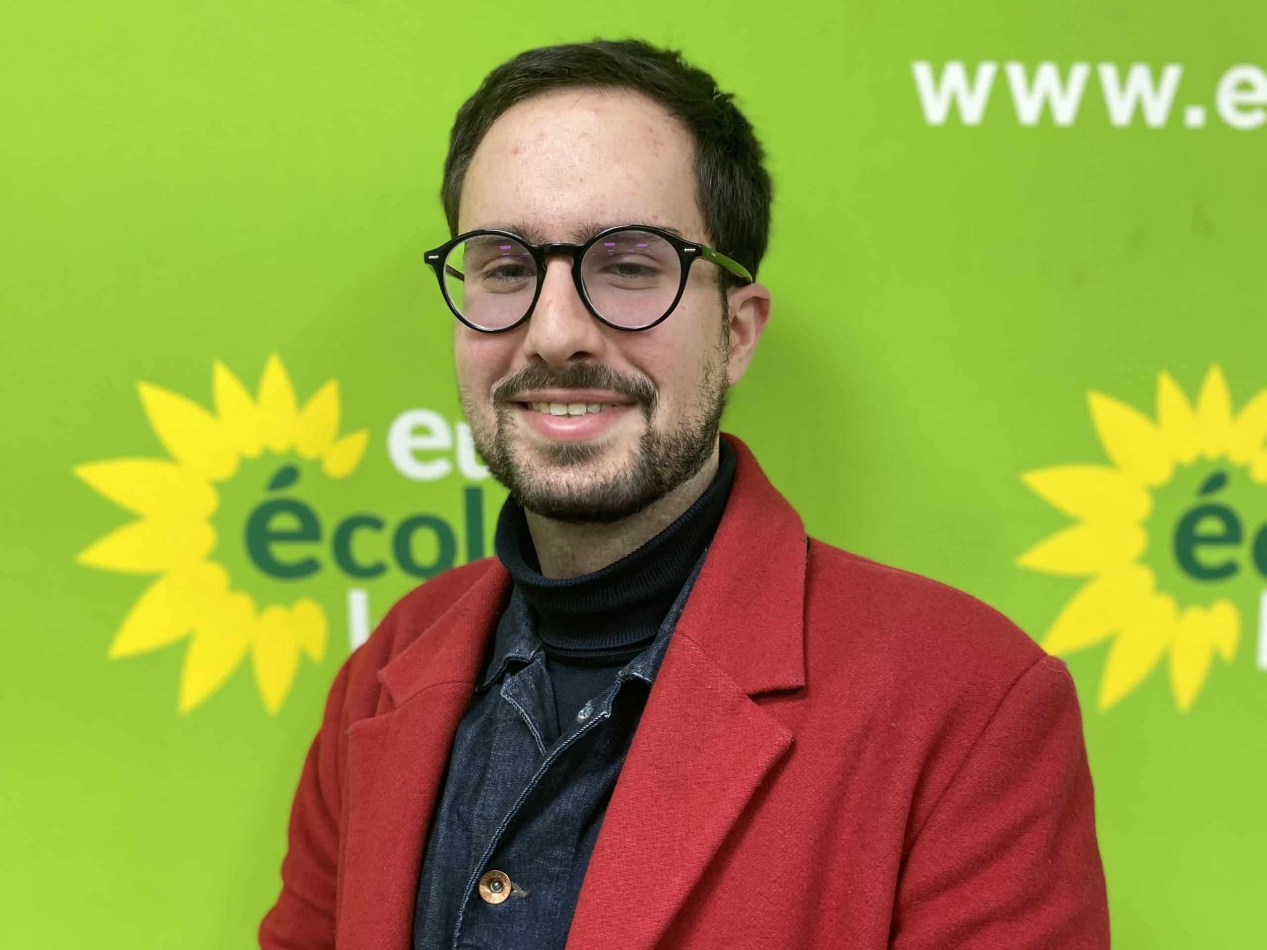 Le trésorier du BED de EELV Paris, Fouad Khayat, souriant en veste rouge, devant un fond vert et jaune aux couleurs de EELV. C'est le responsable du pôle "trésorerie" du BED de EELV Paris.