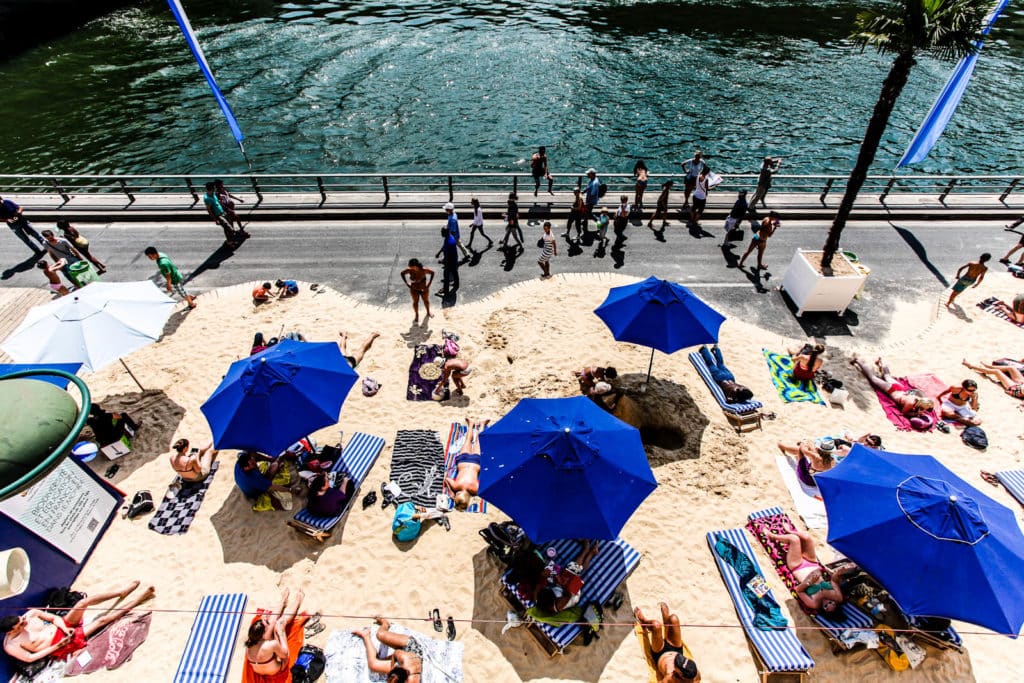 Paris Plage en juillet 2012. On voit la Seine bordée par une plage de sable, avec les parasols et les transats bleus distinctifs.